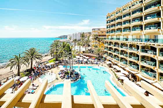 En solrik hotellhage med bassenger, palmer og utsikt over havet. (AI-generert tekst)