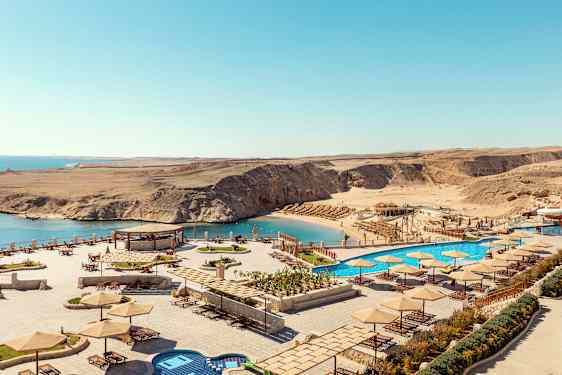 Utsikt over en strand med parasoller og solsenger, samt et basseng ved siden av havet. (AI-generert tekst)