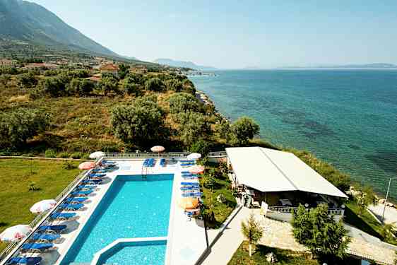 Utendørs basseng med solsenger ved siden av havet, omgitt av grøntområder og bygninger. (AI-generert tekst)