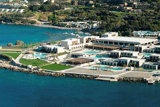 Flyfoto av et hotellkompleks ved kysten, med bassenger og grøntområder. (AI-generert tekst)