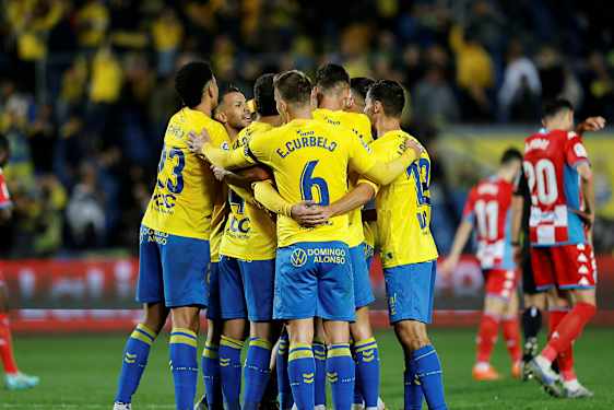 Fotballspillere i gule trøyer klemmer hverandre på banen. (AI-generert tekst)