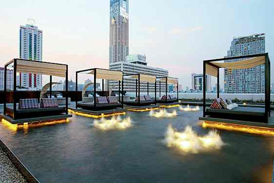 Bilde av en moderne byutsikt med dagsenger plassert over et grunt basseng med lysinstallasjoner i vannet. (AI-generert tekst)