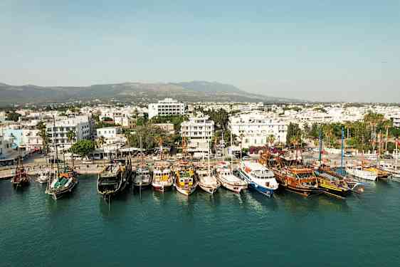 Havnen med flere båter fortøyd og en by med hvite bygninger i bakgrunnen. (AI-generert tekst)