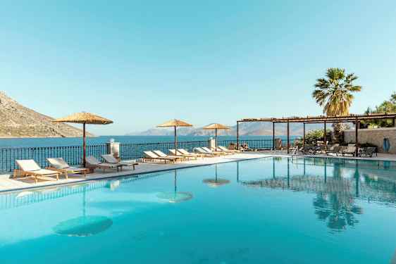 Et utendørs svømmebasseng med solsenger og parasoller ved siden, samt havutsikt i bakgrunnen. (AI-generert tekst)