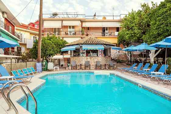 Et utendørs svømmebasseng omgitt av solsenger og parasoller, med en liten kafé i bakgrunnen. (AI-generert tekst)