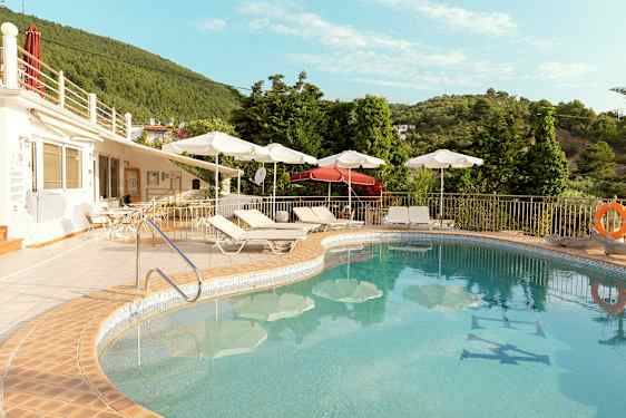 Utendørs svømmebasseng med solsenger og parasoller ved en terrasse i nærheten av grøntområder. (AI-generert tekst)