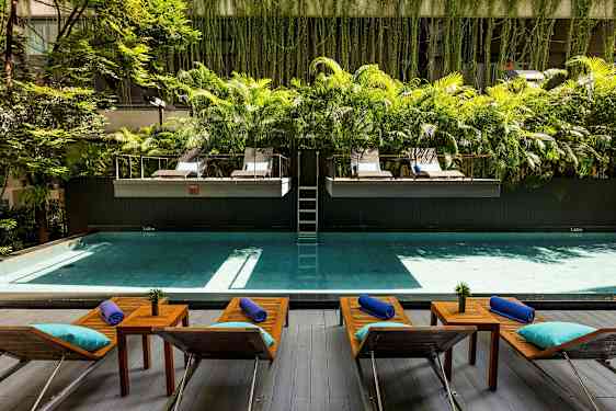 Et basseng med solsenger og bord foran, omgitt av grøntområder og palmer. (AI-generert tekst)