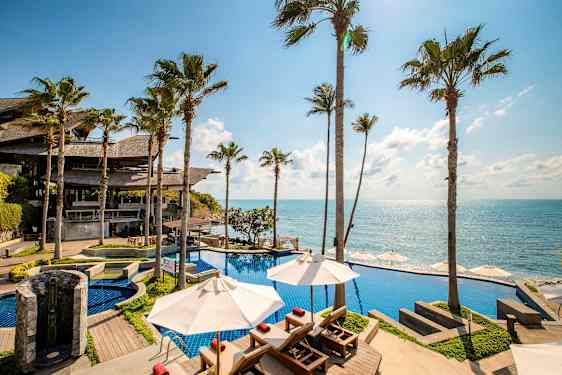 Et bassengområde ved havet med fantastisk utsikt over blått vann, omgitt av høye palmer. (AI-generert tekst)