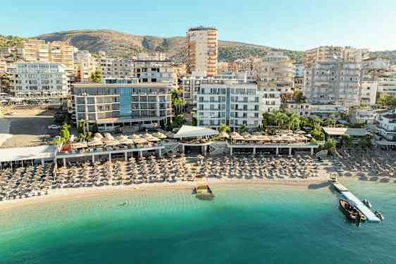 Utsikt over en strand med solsenger og hotellbygninger i bakgrunnen. (AI-generert tekst)