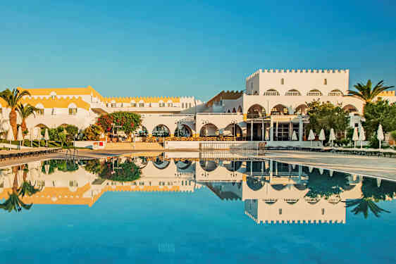 En hvit bygning med gult tak ved et basseng med solsenger og parasoller. (AI-generert tekst)