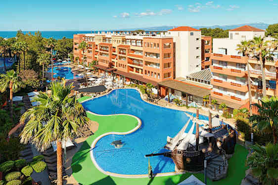 Hotellområde med stort basseng, omgitt av palmer og bygninger. (AI-generert tekst)