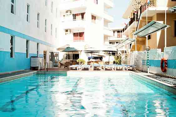 Utendørsbasseng med solsenger og parasoller, omgitt av bygninger. (AI-generert tekst)