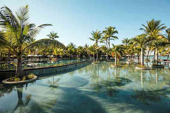 Et stort svømmebasseng omgitt av palmer under en klar blå himmel. (AI-generert tekst)