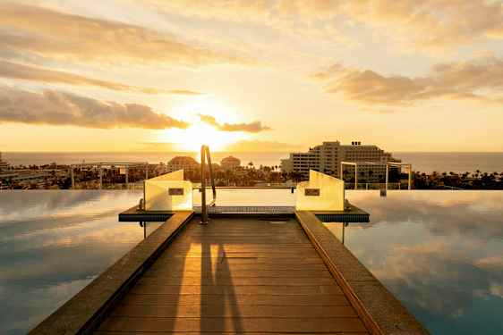 Et infinitybasseng med trebro og utsikt over havet ved solnedgang. (AI-generert tekst)