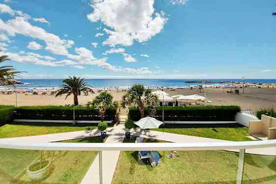 En utsikt fra balkongen med utsikt over en sandstrand, solsenger og parasoller samt havet og himmelen. (AI-generert tekst)