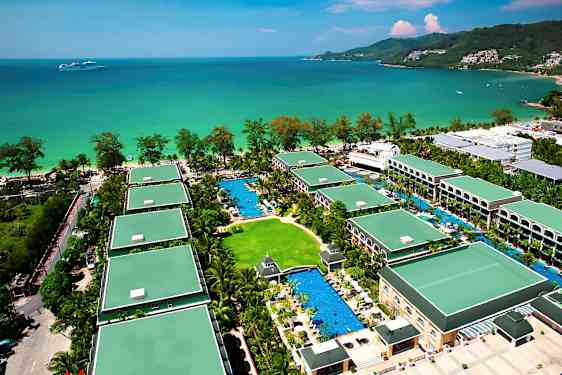 Oversiktsbilde av et feriehotell med flere bygninger omgitt av grøntområder og bassenger, beliggende ved havet. (AI-generert tekst)