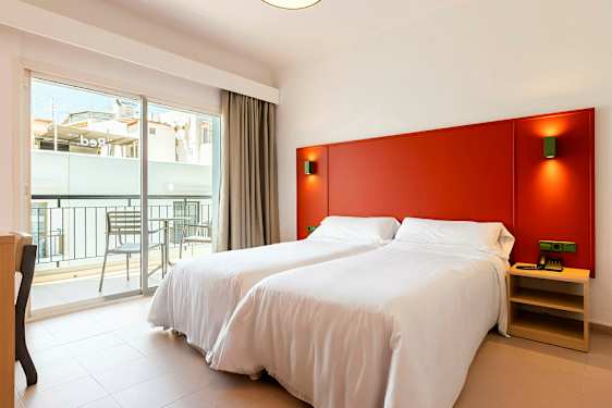 Et rom med to enkeltsenger med hvitt sengetøy, en rød sengegavel og en balkong utenfor. (AI-generert tekst)