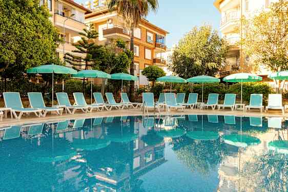 Utendørsbasseng omgitt av solsenger og parasoller, med bygninger i bakgrunnen. (AI-generert tekst)