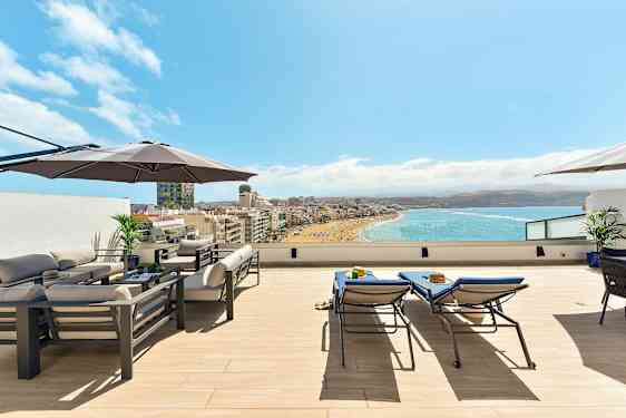 Takterrasse med møbler, parasoll og utsikt over en strand og havet. (AI-generert tekst)
