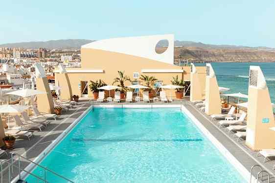 Et takbasseng omgitt av solsenger og parasoller med utsikt over byen og havet. (AI-generert tekst)