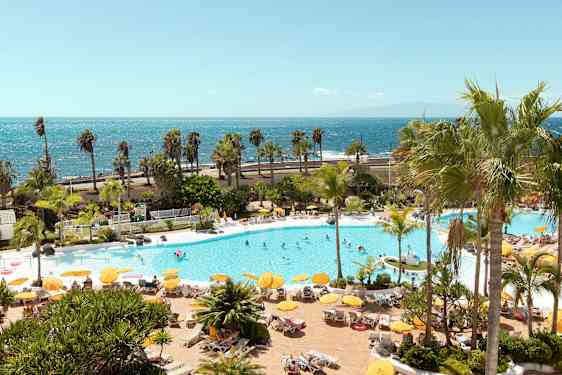 Bassengområde med solsenger, parasoller og mennesker, med havet i bakgrunnen. (AI-generert tekst)