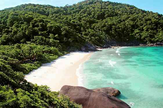 Bilde av en strand omgitt av grønne fjell og blått hav. (AI-generert tekst)