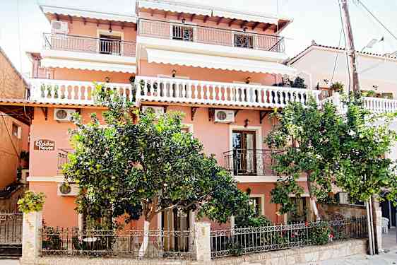 En rosa bygning med balkonger og grønne trær foran. (AI-generert tekst)