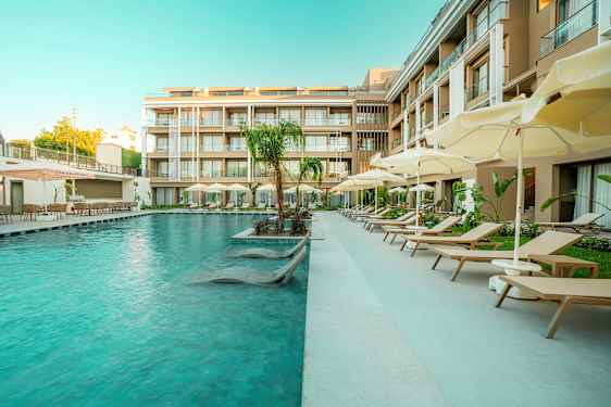 Et hotellbasseng med solsenger og parasoller ved siden av moderne bygninger. (AI-generert tekst)