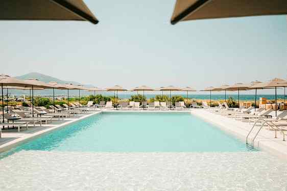 Et utendørs basseng omgitt av solsenger og parasoller, med utsikt over landskap og hav. (AI-generert tekst)