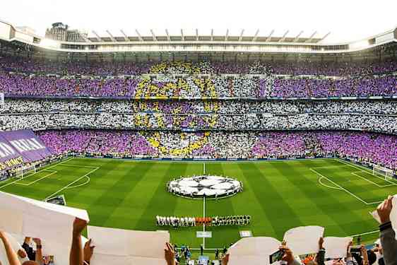 Et fullt fotballstadion med farget publikumsmønster og lag på banen. (AI-generert tekst)