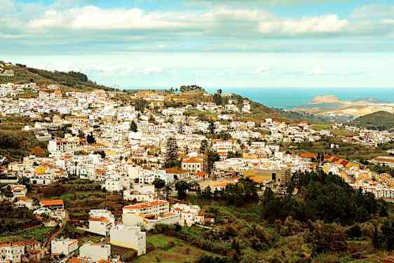 Utsikt over en by med mange hvite bygninger som ligger i en frodig dal nær havet. (AI-generert tekst)
