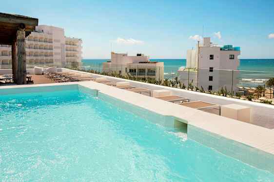 Et basseng med utsikt mot en strand med flere bygninger i bakgrunnen. (AI-generert tekst)