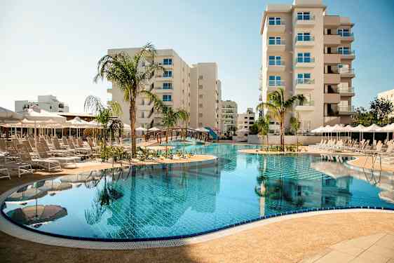 Et utendørs svømmebasseng omgitt av solsenger og parasoller, med høye bygninger i bakgrunnen. (AI-generert tekst)