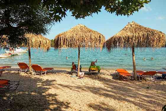 Strand med solsenger og parasoller nær havet, folk svømmer i vannet. (AI-generert tekst)