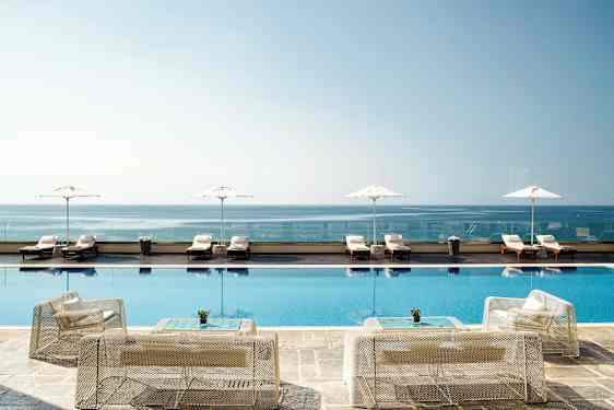 Bilde av et infinitybasseng ved kysten, med solsenger og parasoller i bakgrunnen. (AI-generert tekst)