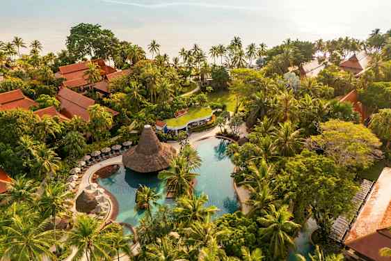 Flyfoto av et tropisk feriested med bassengområde, frodig vegetasjon og tradisjonelt bygde bungalower. (AI-generert tekst)