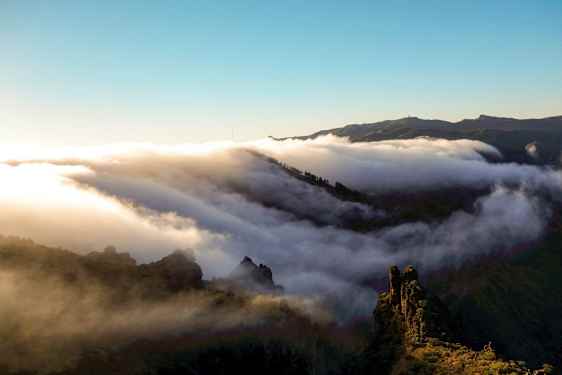 Skyer svever over en fjellkjede ved soloppgang eller solnedgang. (AI-generert tekst)