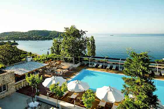 Svømmebasseng med parasoller og utsikt over havet. (AI-generert tekst)