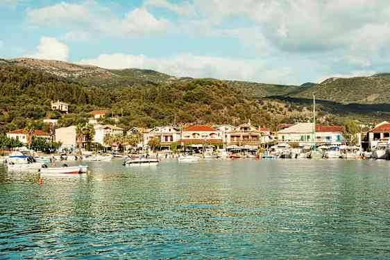 En havsbukt med småbåter og en kystby fylt med hus og trær i bakgrunnen. (AI-generert tekst)