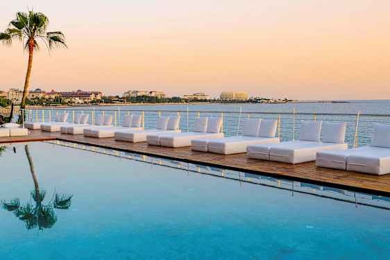 Solstoler ved et basseng med utsikt over havet og bygninger i bakgrunnen. (AI-generert tekst)