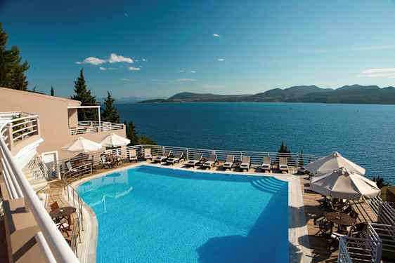 Et utendørs svømmebasseng med solsenger og parasoller, med utsikt over havet og fjell i det fjerne. (AI-generert tekst)