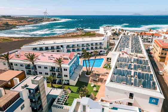 Et hotellresort med basseng, omgitt av bygninger, med utsikt til havet og bølgene. (AI-generert tekst)