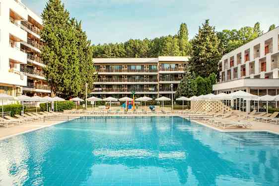 Utendørsbasseng med solsenger og parasoller, omgitt av moderne bygninger og grøntområder. (AI-generert tekst)