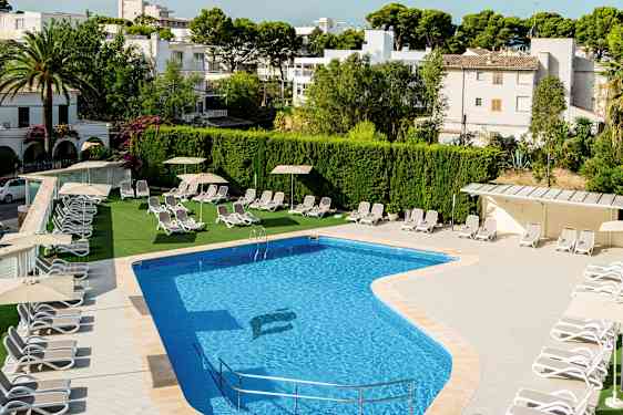 Utendørsbasseng med solsenger og parasoller ved siden, omgitt av grøntområder og bygninger. (AI-generert tekst)