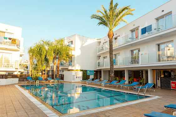 Et utendørsbasseng omgitt av solsenger og hvite bygninger. (AI-generert tekst)