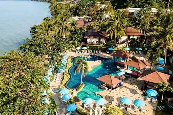 Et feriested med basseng, palmer og parasoller ved sjøen. (AI-generert tekst)