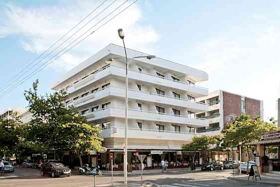 Fire etasjer høyt, hvitt hotell med balkonger. Under bygningen finnes en restaurant. (AI-generert tekst)