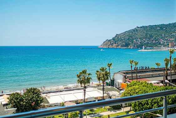 Utsikt over havet og en strand med bygninger i forgrunnen. En odde med bebyggelse er synlig i bakgrunnen. (AI-generert tekst)