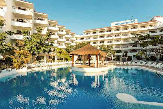 Hotellkompleks med flere etasjer, et stort basseng og en takhyttestruktur i midten av bassenget. (AI-generert tekst)