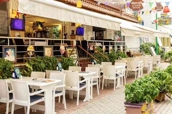 Restaurant med uteservering med hvite bord og stoler ved et hotell. (AI-generert tekst)